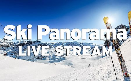 Ski resort with mountain panorama in front of a bright blue sky, chairlift, slopes with skiers and a pair of skis with poles set up on the slope. The image is labeled with the white lettering "Ski Panorama Live Stream".