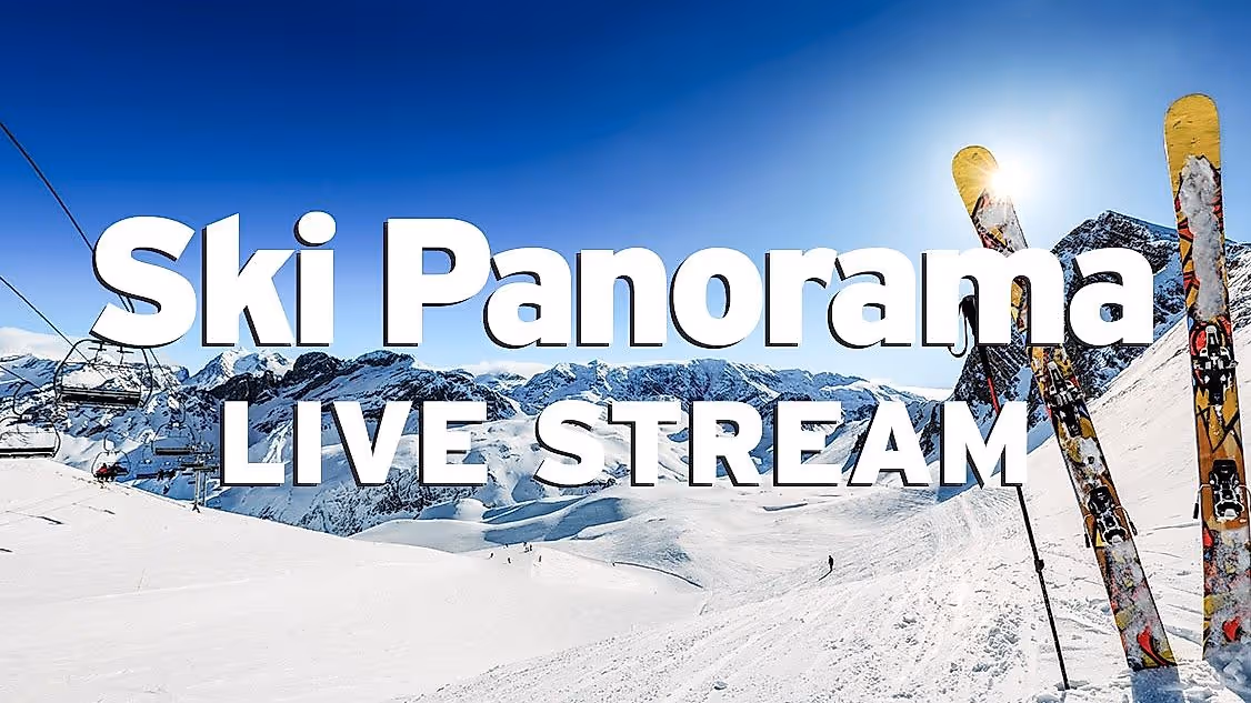 Skigebiet mit Bergpanorama vor strahlend blauem Himmel, Sessellift, Pisten mit Skifahrern und einem paar Ski mit Stöcken, das auf der Piste aufgestellt ist. Das Bild ist mit dem weißen Schriftzug "Ski Panorama Live Stream" beschriftet.