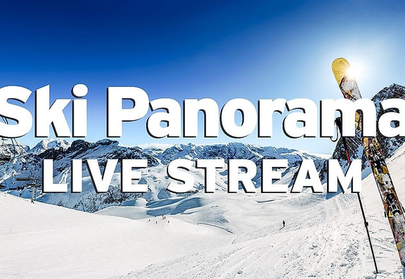 Skigebiet mit Bergpanorama vor strahlend blauem Himmel, Sessellift, Pisten mit Skifahrern und einem paar Ski mit Stöcken, das auf der Piste aufgestellt ist. Das Bild ist mit dem weißen Schriftzug "Ski Panorama Live Stream" beschriftet.